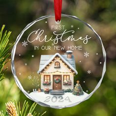 a christmas ornament hanging from a tree with a house in the snow on it