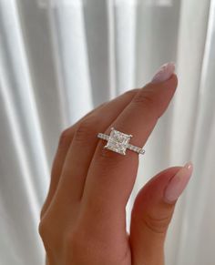 a woman's hand with a diamond ring on top of her finger, in front of a white curtain