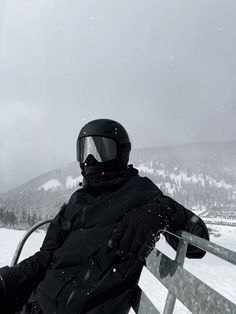 a person sitting in the snow wearing a helmet and goggles on top of a fence