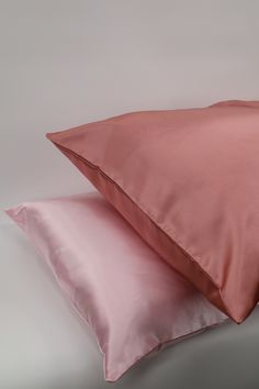 two pink pillows sitting next to each other on top of a white surface with a gray background