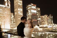 a bride and groom standing in front of the city skyline at night