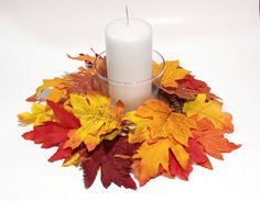 a white candle surrounded by autumn leaves