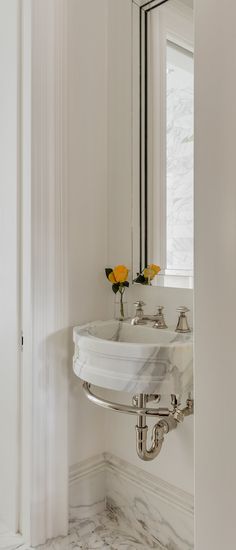 a bathroom sink sitting under a mirror next to a wall mounted faucet with flowers in it