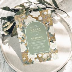 the wedding stationery is sitting on top of a silver platter with greenery