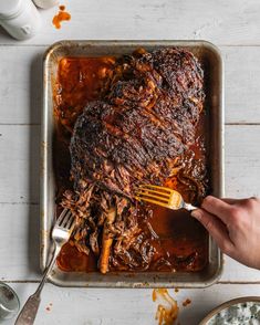 a person is holding a fork over a roasting pan filled with ribs