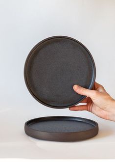 a hand holding a black plate on top of a white table next to a round tray