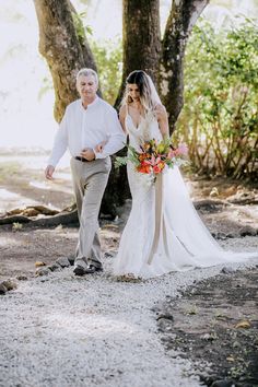 a bride and groom walking through the woods