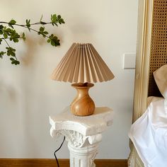 a lamp sitting on top of a white table next to a bed with sheets and pillows