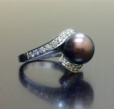 a black pearl and diamond ring sitting on top of a table