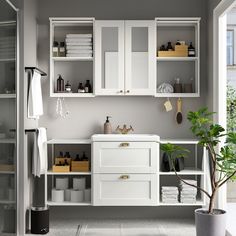 a bathroom with white cabinets and drawers next to a potted plant