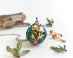 a glass ball necklace with flowers and leaves on the inside is surrounded by other items