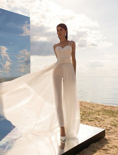 a woman standing on top of a beach next to the ocean wearing a white dress