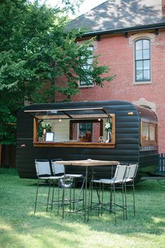 an old trailer converted into a house with chairs and table in the grass next to it