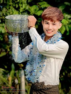 a young man wearing a lei and holding a bowl with water pouring out of it