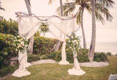 an outdoor wedding setup with white flowers and greenery on the grass near palm trees