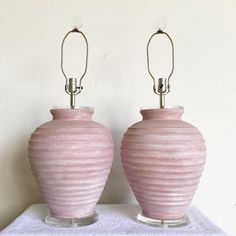 two pink vases sitting next to each other on top of a white cloth covered table