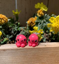 two little pink plastic animals sitting on top of a wooden table next to yellow flowers