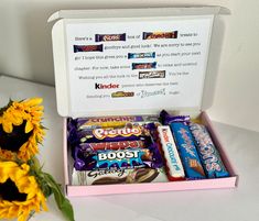 a pink box filled with candy and sunflowers next to a white table top