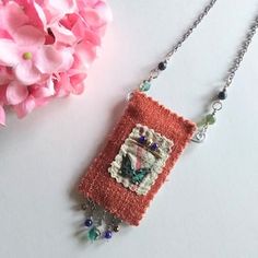 a close up of a necklace on a table next to pink flowers and a flower pot