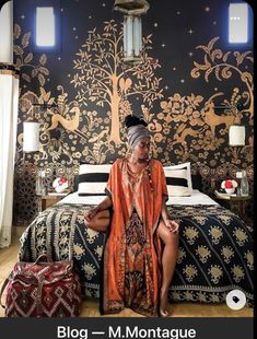 a woman sitting on top of a bed in front of a tree wallpapered bedroom