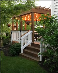 a white deck with lights on it and stairs leading up to the top level, surrounded by greenery