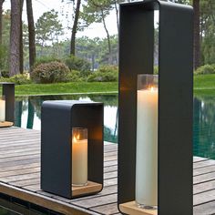 two lit candles sitting on top of a wooden dock next to a swimming pool with trees in the background