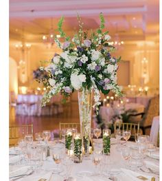 a tall vase filled with white and purple flowers sitting on top of a dining room table