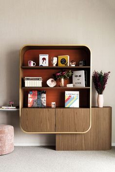 a wooden book shelf with books on it next to a pink stool and potted plant