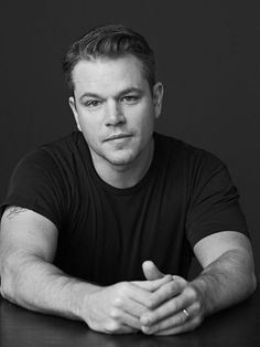 a black and white photo of a man sitting at a table with his arms crossed