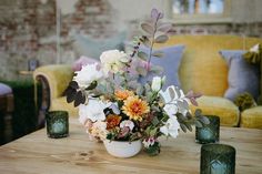 a vase filled with lots of flowers sitting on top of a wooden table next to candles