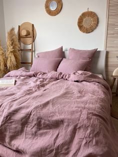 a bed with pink linens and pillows in a white room next to wicker baskets