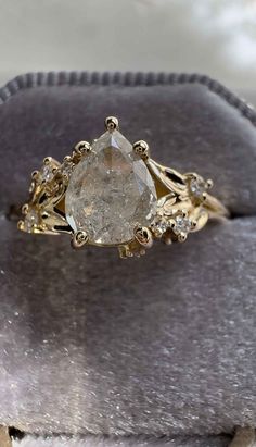 an engagement ring with a pear shaped diamond in the center on top of a velvet box