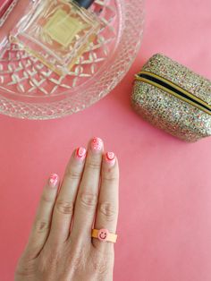 a woman's hand with pink and white nail polish on it next to a bag