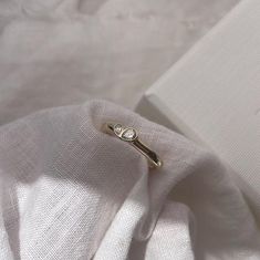 a gold ring sitting on top of a white cloth next to an open box with a diamond in it