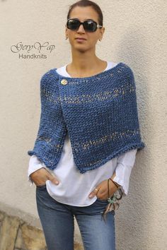 a woman standing next to a white wall wearing a blue knitted sweater and jeans