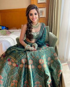 a woman sitting in a chair wearing a green and gold lehenga with matching jewelry