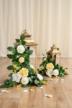 two gold lanterns with white flowers and greenery on the floor next to each other