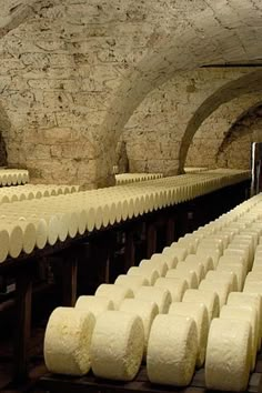 several rows of cheese stacked on top of each other in a room with stone walls