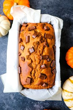 a loaf of chocolate chip pumpkin bread in a white wrapper next to mini pumpkins