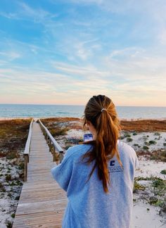 a woman standing on a boardwalk looking out at the ocean and sand with blue skies