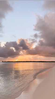 the sun is setting over the water and clouds are reflected in the calm ocean waters