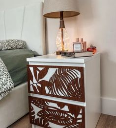 a night stand with a lamp on it next to a bed and a white headboard