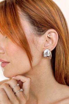 a woman with red hair is wearing two silver rings on her left ear and the other half of her neck