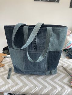 a denim tote bag sitting on top of a white and gray tablecloth covered bed