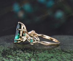 a gold ring with an emerald stone and leaves on the side, sitting on top of a green rock