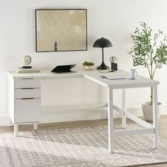 a white desk sitting on top of a wooden floor next to a potted plant