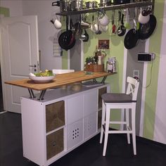 a kitchen island with two stools and pots on the rack above it, in front of a green wall