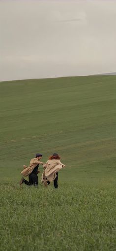 two people are running in the grass with one holding his coat over his head and the other facing him