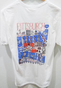 a white t - shirt with the words pittsburgh on it hanging from a wooden hanger