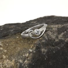 The so-called "whiplash line" is one of the defining hallmarks of the Art Nouveau style. Here, the whiplash curves in a graceful arabesque around a sparkling gemstone and entwines around your finger. The Arabesque Ring is dainty and elegant when worn alone; but this slender stacking ring is designed to nestle closely with one or more accompanying bands. This sparkly white sapphire and sterling silver ring is handcrafted and made to order. Wear it by itself, or customize a stack of skinny bands a Elegant Sterling Silver Ring With Single Diamond, Elegant Bypass Ring With Tension Setting For Formal Occasions, Elegant Birthstone Ring With Round Gemstone, Elegant Birthstone Ring With Gemstone, Elegant Anniversary Birthstone Ring With Tension Setting, Elegant Amethyst Birthstone Ring For Anniversary, Diamond Jewelry With Tension Setting And Modern Twist, Modern Diamond Jewelry With Tension Setting, Modern Twist Diamond Jewelry With Tension Setting